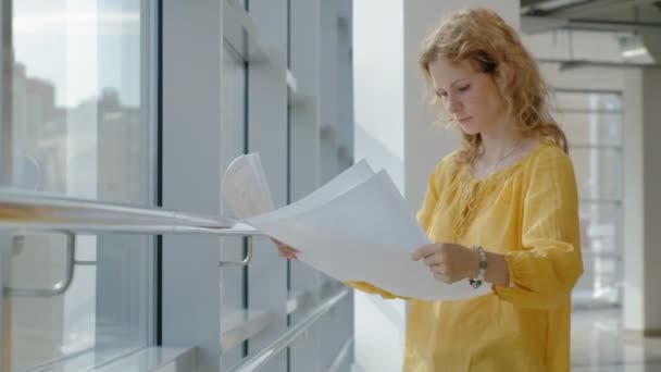 Mulher de negócios bonita jovem, pela janela com um escaneia um desenho em papel — Vídeo de Stock