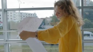 Genç güzel iş kadını, bir çizim kağıt üzerinde inceden inceye gözden geçirmek ile pencere tarafından