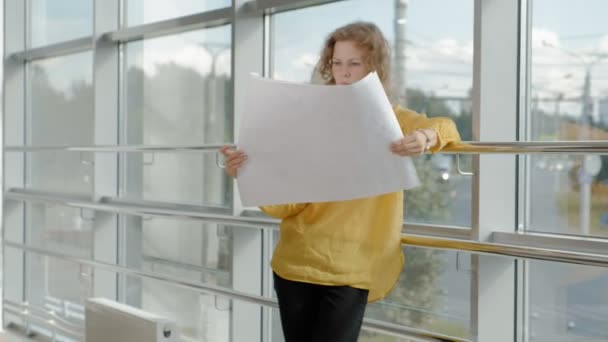 Fiatal szép üzletasszony, az ablak-val egy vizsgál egy rajz papírra — Stock videók