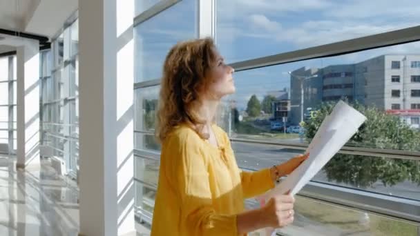 Joven mujer de negocios hermosa, junto a la ventana con un escaneo de un dibujo en papel — Vídeos de Stock