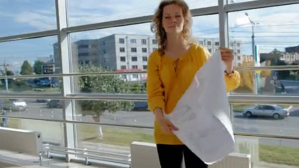 Jonge mooie zakenvrouw, bij het raam met een scans een tekening op papier — Stockvideo