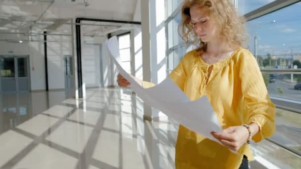 Mulher de negócios bonita jovem, pela janela com um escaneia um desenho em papel — Vídeo de Stock