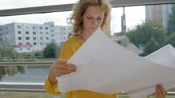 Joven mujer de negocios hermosa, junto a la ventana con un escaneo de un dibujo en papel — Vídeos de Stock