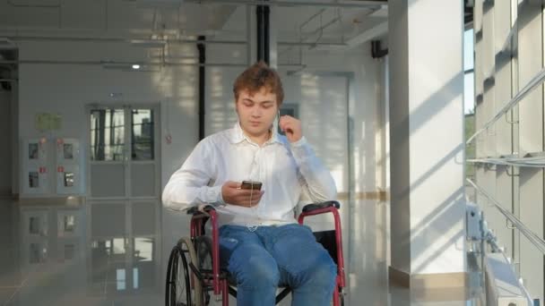 Un handicapé en fauteuil roulant à une fenêtre écoutant de la musique sur un casque à partir d'un smartphone — Video