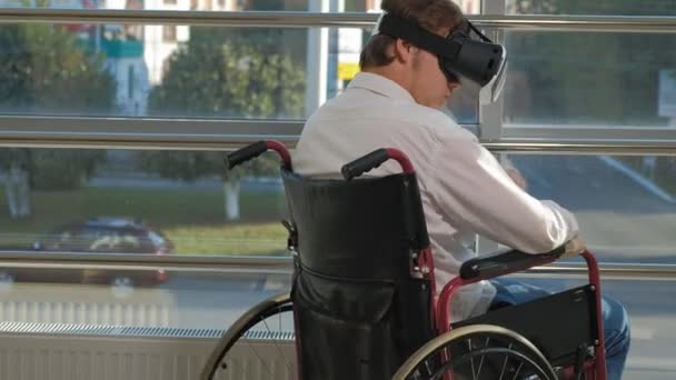 Uomo disabile su una sedia a rotelle ad una finestra utilizza un casco di realtà virtuale — Video Stock