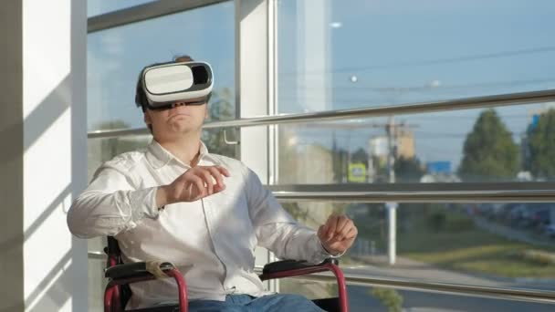 Funksjonshemmet mann i rullestol ved et vindu bruker en hjelm av virtuell virkelighet – stockvideo