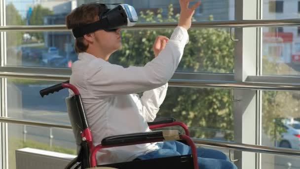 Инвалид на инвалидной коляске у окна использует шлем виртуальной реальности — стоковое видео