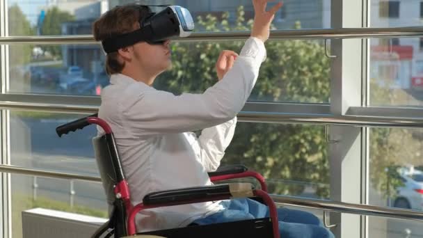 Uomo disabile su una sedia a rotelle ad una finestra utilizza un casco di realtà virtuale — Video Stock