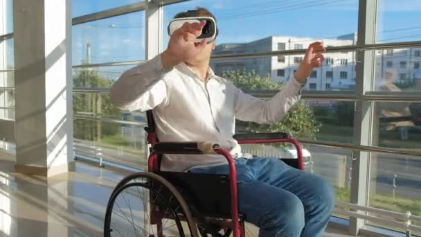 窓際で車椅子に無効になっている男は、バーチャルリアリティのヘルメットを使用してください。 — ストック動画