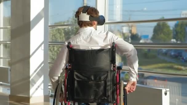 Disabled man on a wheelchair at a window uses a helmet of virtual reality — Stock Video