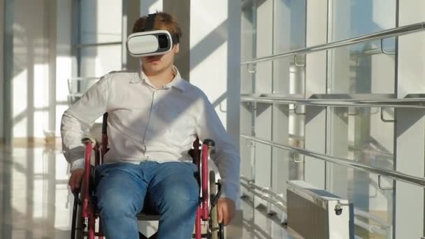 Инвалид на инвалидной коляске у окна использует шлем виртуальной реальности — стоковое видео