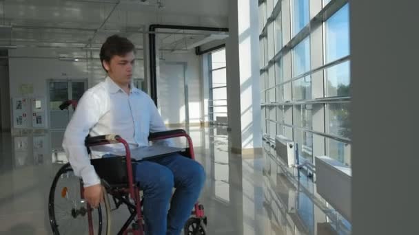 Hombre de negocios discapacitado en una silla de ruedas en una ventana con un ordenador portátil — Vídeo de stock