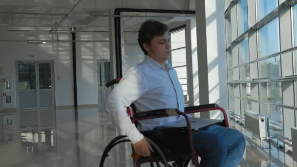 Hombre de negocios discapacitado en una silla de ruedas en una ventana con un ordenador portátil — Vídeos de Stock