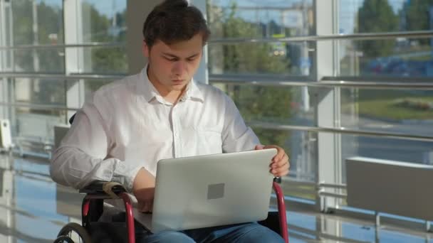 Empresário deficiente em uma cadeira de rodas em uma janela com um laptop — Vídeo de Stock