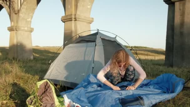 Jonge vrouw verzamelt een toeristische tent in de buurt van de oude brug — Stockvideo