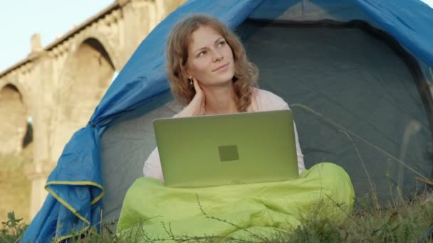 Jovem mulher trabalhando atrás de um laptop em uma tenda turística perto da ponte velha — Vídeo de Stock