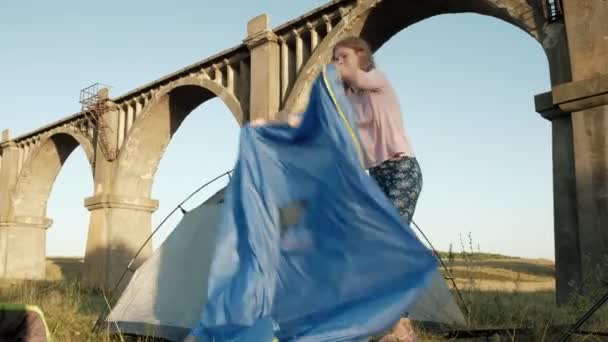 Jeune femme recueille une tente touristique près du vieux pont — Video