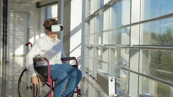 Disabled man on a wheelchair at a window uses a helmet of virtual reality — Stock Video