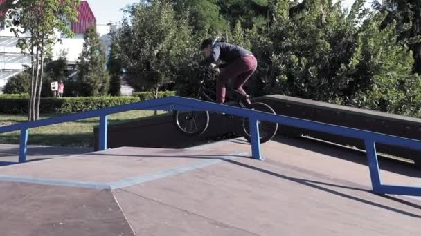 Un niño está montando trucos de ciclismo BMX en un parque de skate en un día soleado. Super cámara lenta — Vídeo de stock