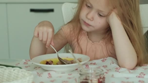 Menina bonita feliz comer mingau de cereal para o café da manhã e se divertir na cozinha branca em casa — Vídeo de Stock