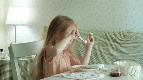 Щаслива красива дівчина їсть кашу на сніданок і розважається на білій кухні вдома — стокове відео