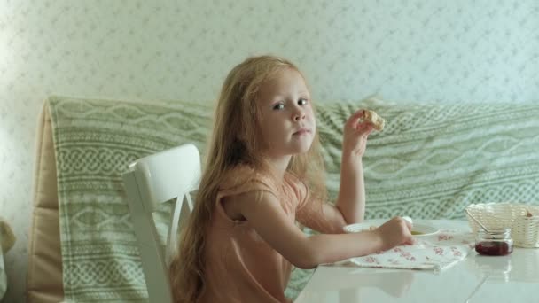 Heureuse belle fille manger du porridge pour le petit déjeuner et s'amuser dans la cuisine blanche à la maison — Video