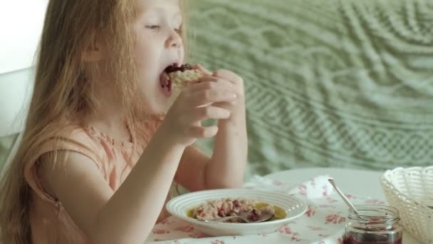 Menina bonita feliz comer mingau de cereal para o café da manhã e se divertir na cozinha branca em casa — Vídeo de Stock