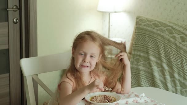 Feliz hermosa chica comiendo gachas para el desayuno y divertirse en la cocina blanca en casa — Vídeos de Stock
