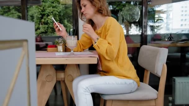 Una hermosa joven bebe un batido en un café. — Vídeos de Stock