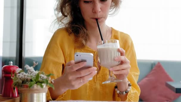Uma bela jovem bebe um smoothie smoothie em um café — Vídeo de Stock