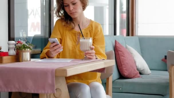 Een mooie jonge vrouw drinken een smoothie smoothie in een café — Stockvideo