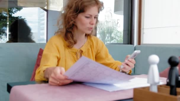 Mooie jonge vrouw die bladeren van documenten in een café — Stockvideo