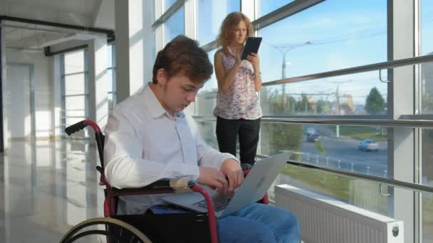 女性近くのラップトップでウィンドウで車椅子の障害者実業家が タブレットを使ってください — ストック動画