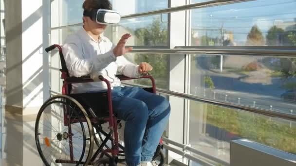 Deficiente homem em uma cadeira de rodas em uma janela usa um capacete de realidade virtual — Vídeo de Stock