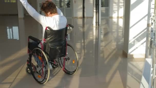 Disabled man on a wheelchair at a window listening to music on headphones from a smartphone — Stock Video