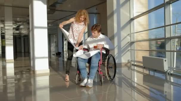 Disabled businessman on a wheelchair in a window with a picture on a large sheet of paper discussing work with a business woman, discussion in the office... — Stock Video