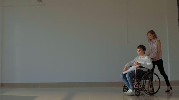 Hombre de negocios discapacitado en una silla de ruedas en una ventana con una imagen en una hoja grande de papel discutir el trabajo con una mujer de negocios, discusión en la oficina ... — Vídeos de Stock