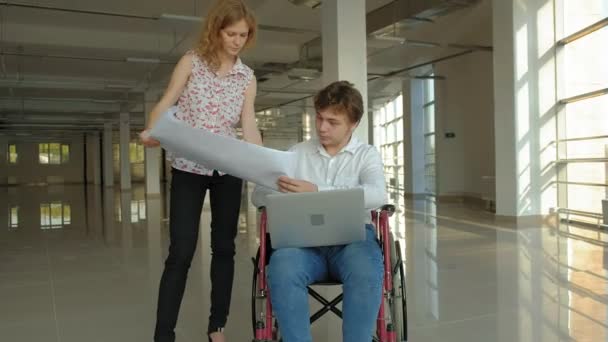 Uomo d'affari disabile su una sedia a rotelle in una finestra con una foto su un grande foglio di carta che discute di lavoro con una donna d'affari, discussione in ufficio ... — Video Stock