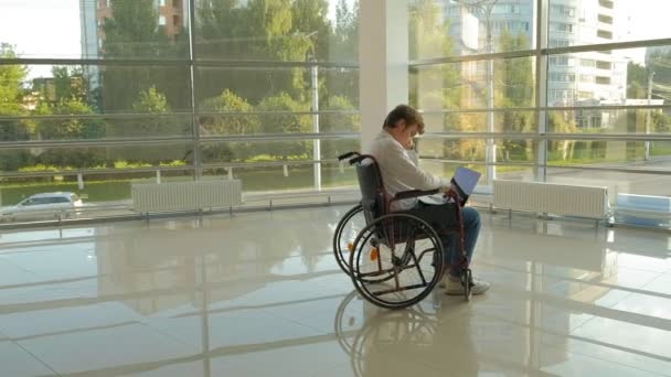 A disabled businessman on a wheelchair in a window with a drawing on a large sheet of paper, discusses work by phone — Stock Video