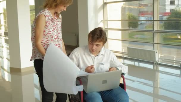 Zakenman op een rolstoel in een venster met een afbeelding op een groot vel papier werk met een zakenvrouw, discussie in het Bureau bespreken uitgeschakeld... — Stockvideo