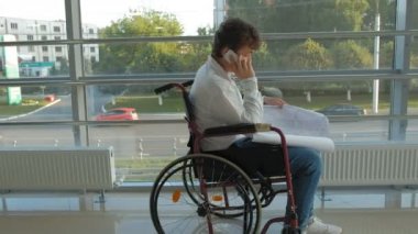 bir pencere, bir tekerlekli sandalye üzerinde Engelli işadamı smartphone kullanır
