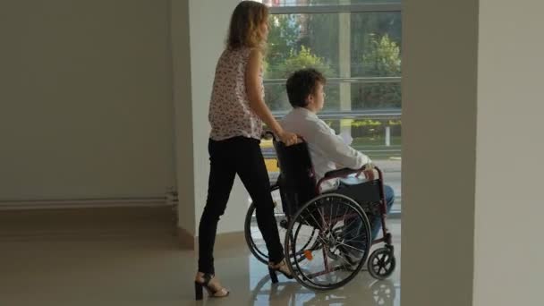 Деловая женщина катит инвалидное кресло с инвалидом-бизнесменом на инвалидной коляске, который разговаривает по телефону — стоковое видео