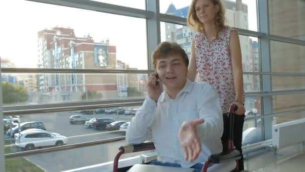 Mujer de negocios que rueda una silla de ruedas con un hombre de negocios discapacitado en una silla de ruedas que está hablando por teléfono — Vídeos de Stock