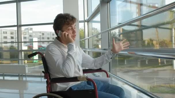 Hombre de negocios discapacitado en una silla de ruedas en una ventana utiliza teléfono inteligente — Vídeos de Stock