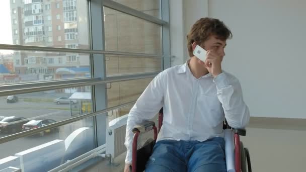 Disabled businessman on a wheelchair at a window uses smartphone — Stock Video