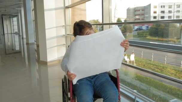 大きな紙の上に描画してウィンドウで車椅子の障害者実業家が電話での仕事を説明します。 — ストック動画