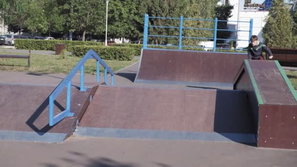 Un niño está montando trucos de ciclismo BMX en un parque de skate en un día soleado. Super cámara lenta — Vídeos de Stock