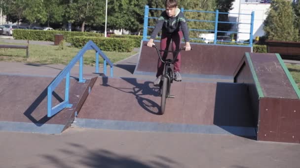 Un niño está montando trucos de ciclismo BMX en un parque de skate en un día soleado. Super cámara lenta — Vídeos de Stock