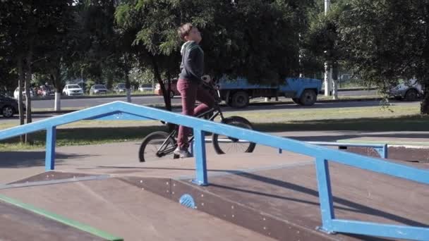 Un niño está montando trucos de ciclismo BMX en un parque de skate en un día soleado. Super cámara lenta — Vídeos de Stock