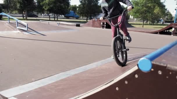 Un niño está montando trucos de ciclismo BMX en un parque de skate en un día soleado. Super cámara lenta — Vídeos de Stock